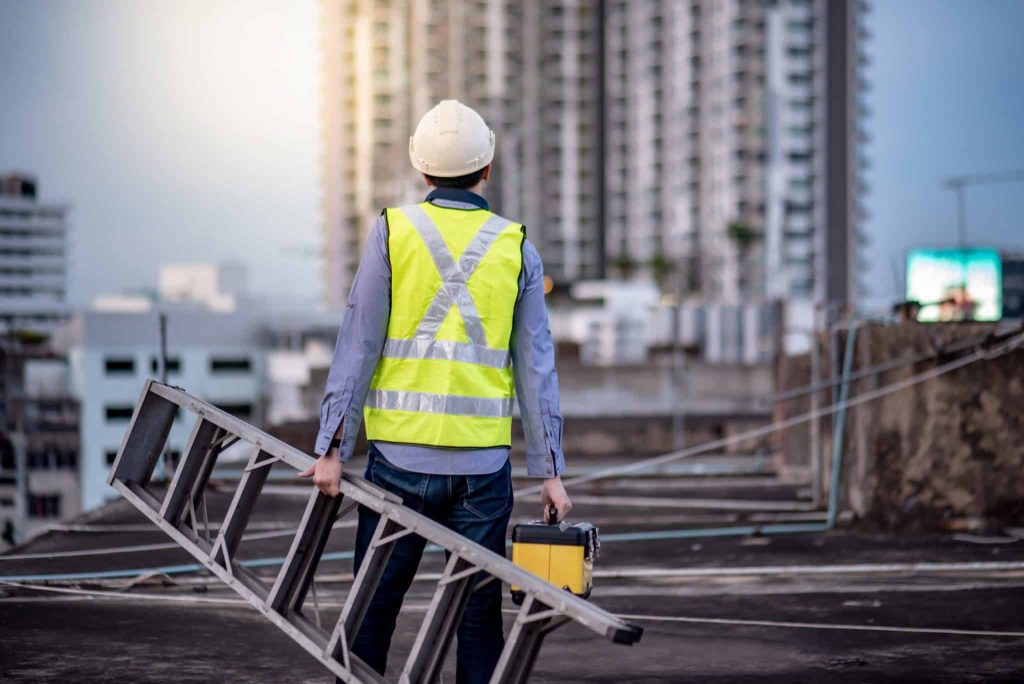 Construction worker with ladder and toolbox on rooftop.