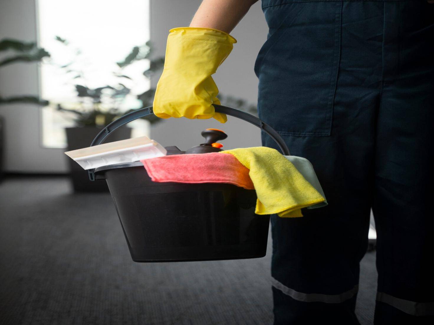 Person holding cleaning bucket with gloves and cloths
