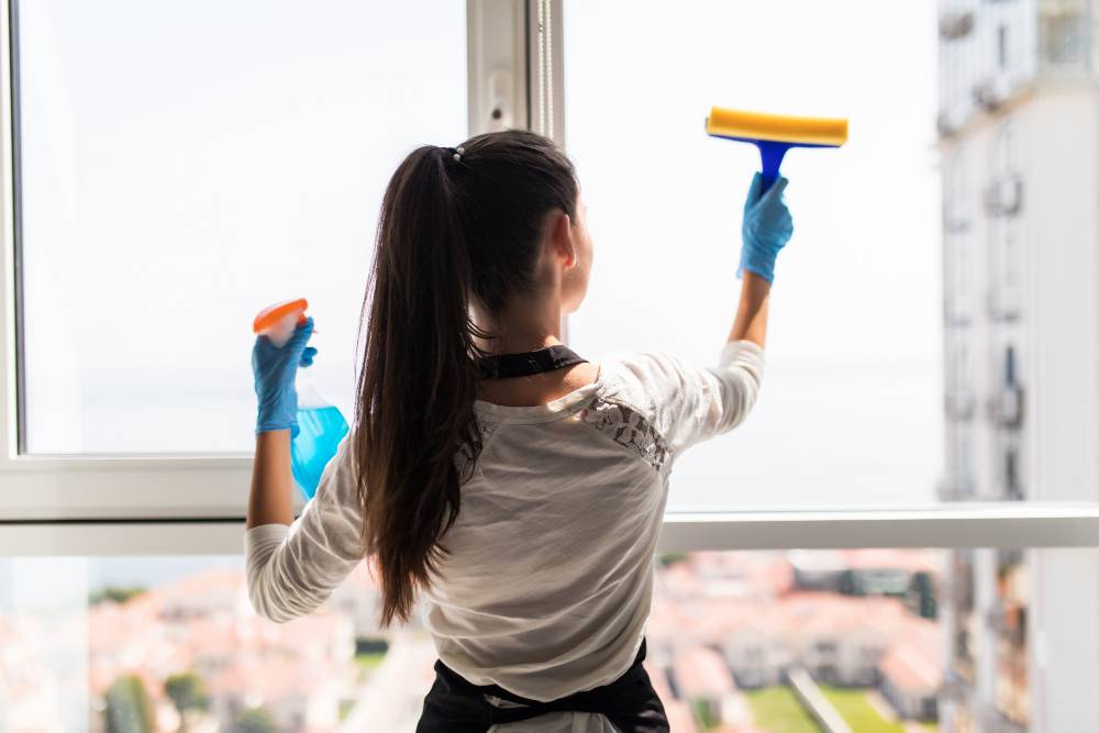 Woman cleaning window with squeegee and spray bottle.