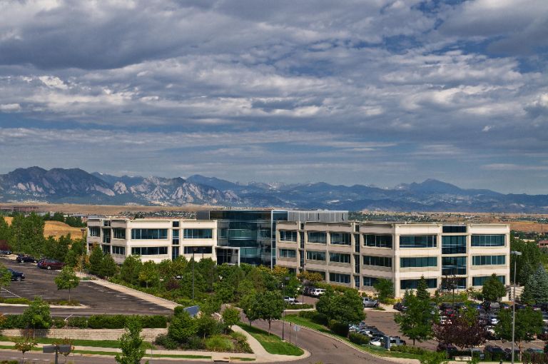 Office building with mountain backdrop under cloudy sky.