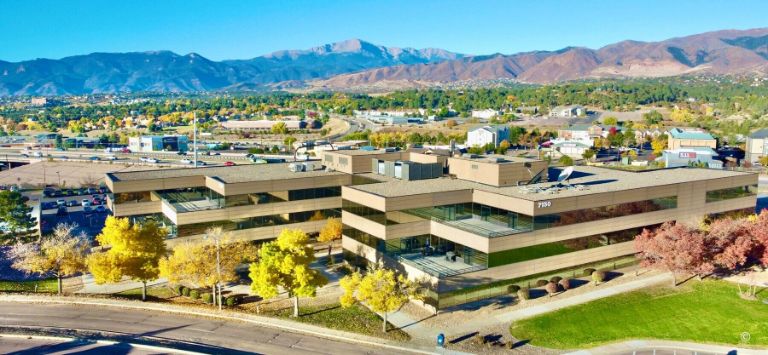 Office building with mountain backdrop and autumn trees.